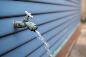 Exterior faucet A faucet running water next to the panel of a house