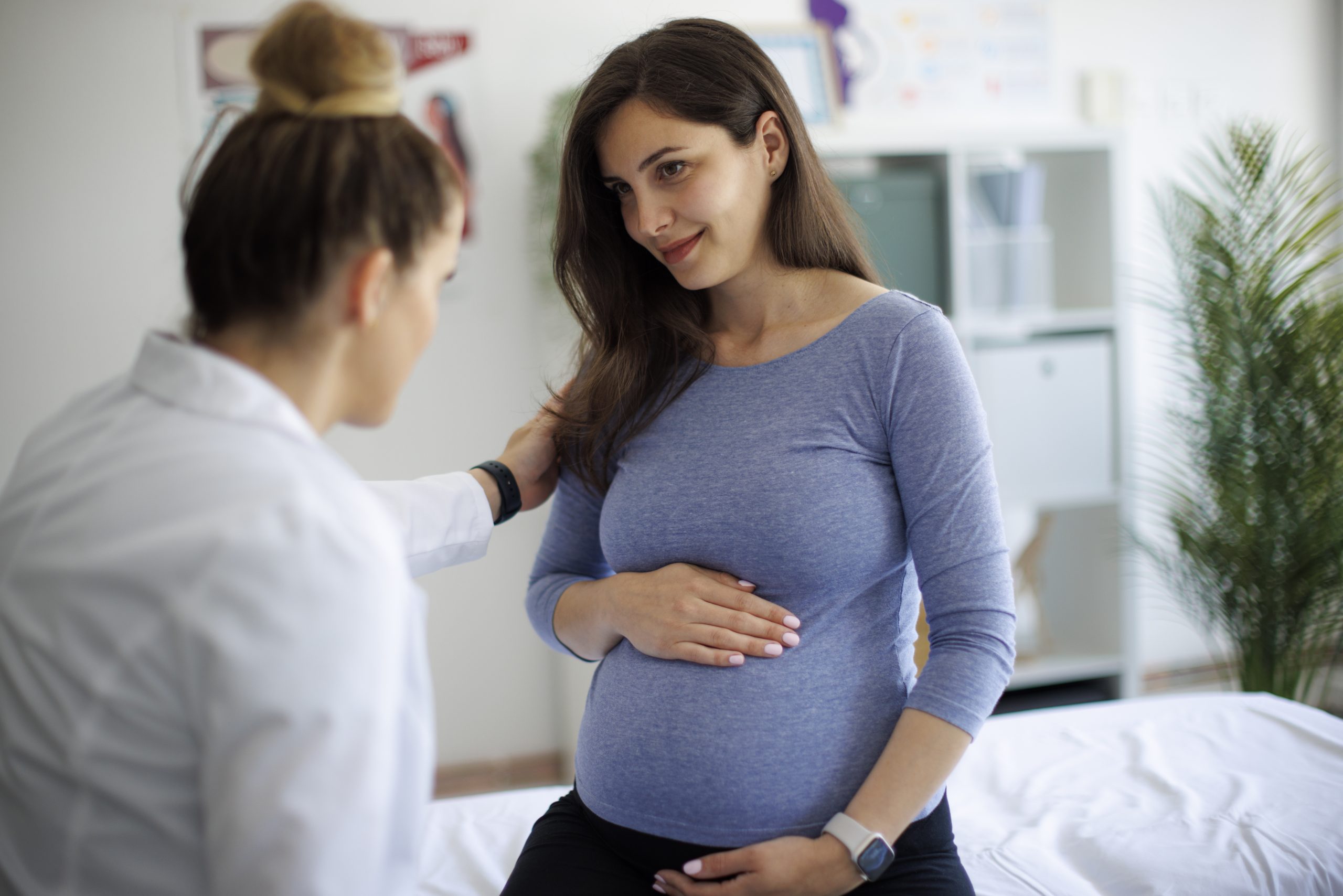 At Risk Pregnant person holding their stomach with their hand speaking to a doctor.
