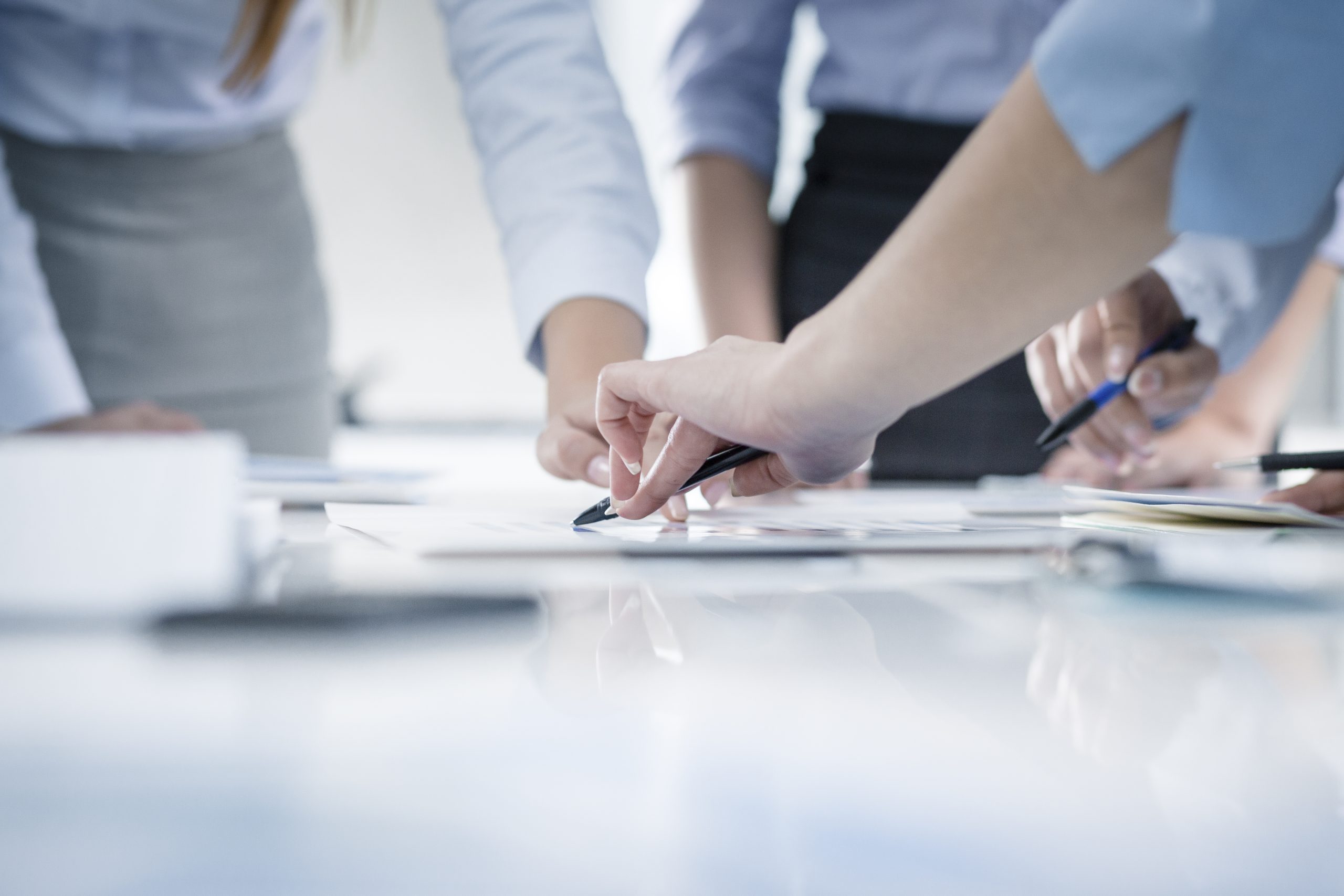 — title missing — Group of people gathered around documents on a table with only their hands visible.