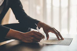 — title missing — A woman's hands holding a pen and writing on a document.