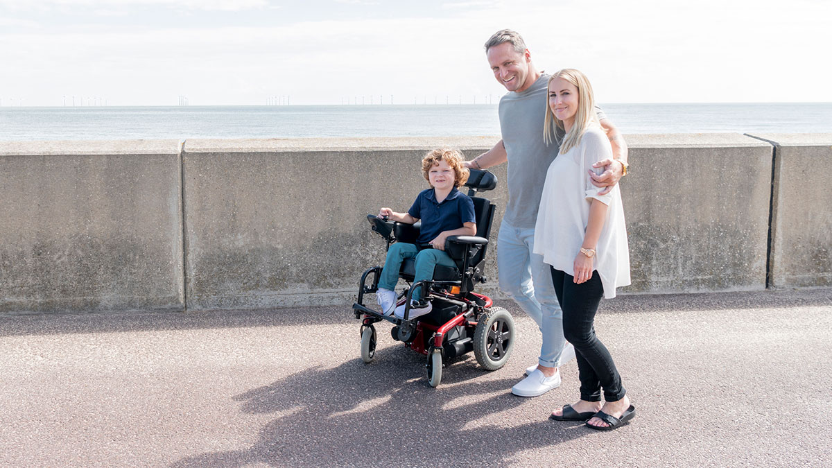 A boy with MD and his family A boy with muscular dystrophy in a wheelchair, with his family next to him.