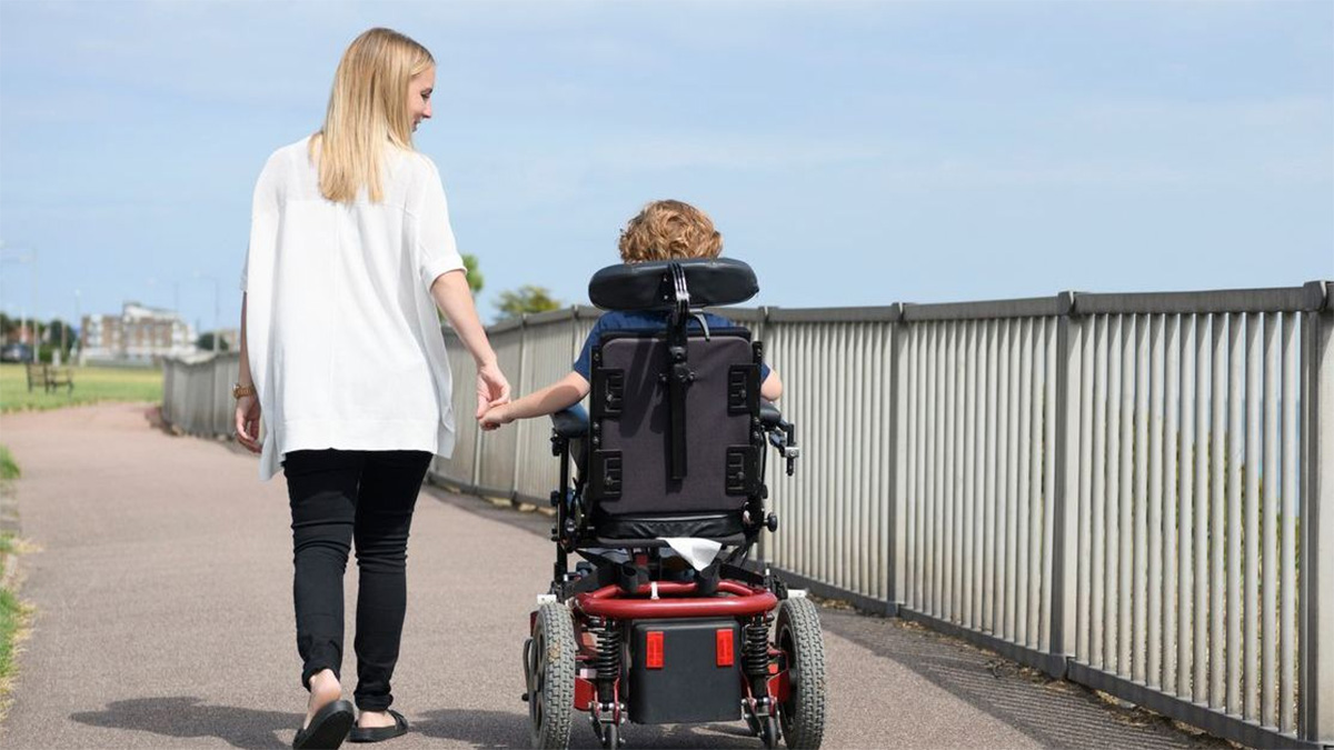 Mom walking with son in wheelchair A mom holds hand and walks with her son in a wheelchair