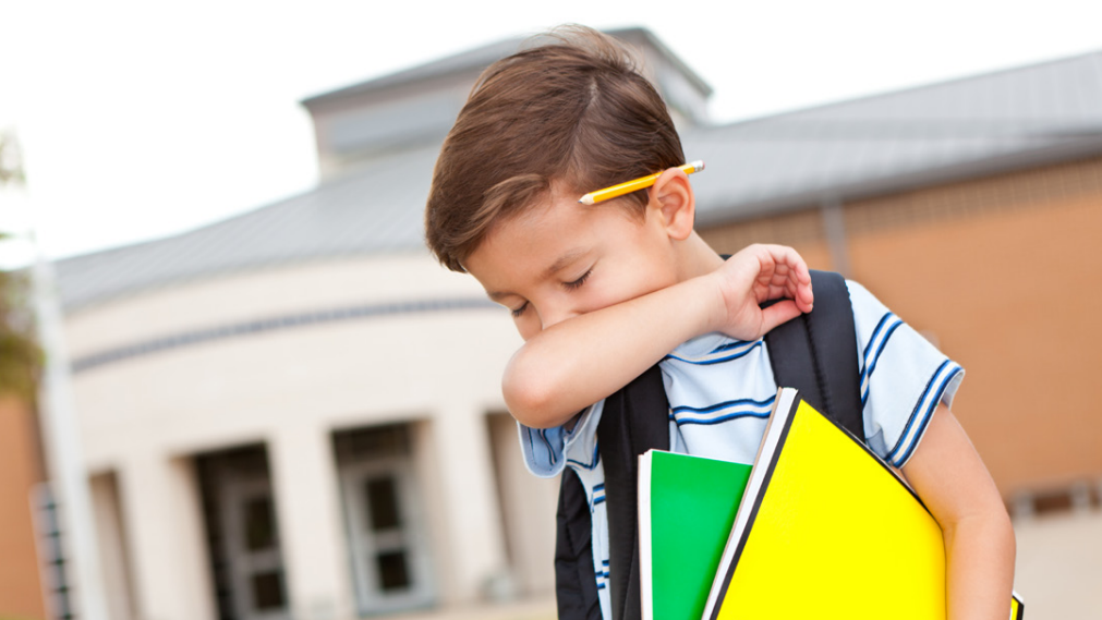 Young boy at school A young boy covers his cough in his elbow while leaving school.
