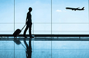 istock-travel-120px.jpg Silhouette of a traveler in an airport, walking with a rolling suitcase behind them as a plane takes off in the background.
