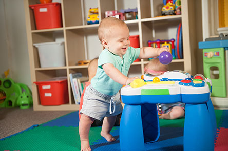 9 Months_Stands, holding on-444px Baby standing and playing with toy