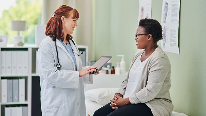 NHIS-Adult-Exam-Physician Doctor standing and talking to her patient who is sitting on the exam table