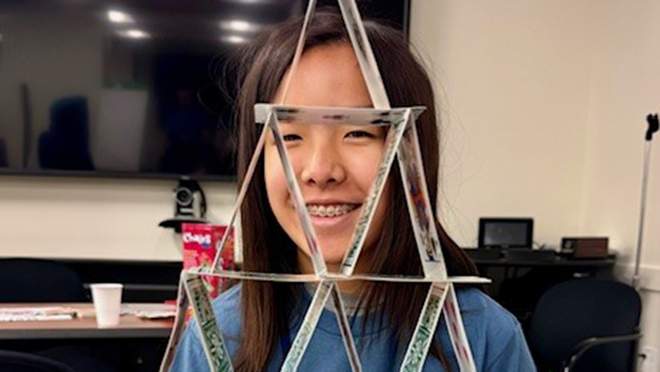 Data Detectives Candid Young asian girl stands behind a house triangle formed by balancing playing cards