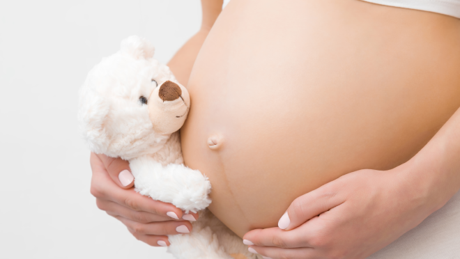 Hand clasping teddy bear next to pregnant abdomen
