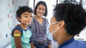 Boy_Mom_Nurse_Bandaid3 Young boy with Band-Aid on his arm sitting next to mother in exam room and smiling at doctor