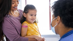 Girl_Mom_Nurse_Bandaid1 Mom holding preschool-age girl with Band-Aid on her arm as they talk to doctor in exam room