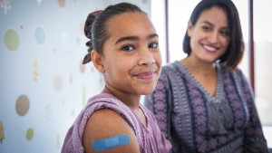 Girl_Mom_Nurse_Bandaid3 Girl looking at camera smiling with Band-Aid on her arm as mom looks at her