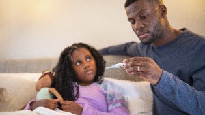 SickChild_DadTakingTemp Young girl sick in bed with dad taking her temperature and looking at thermometer