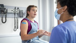 Teen_Girl_Nurse Teenage girl with bandaid on arm talking with doctor who is wearing a mask