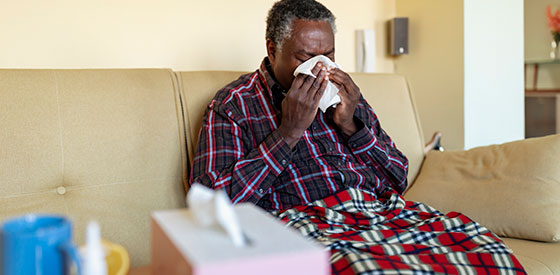 man-blowing-nose Man sitting on couch blowing his nose
