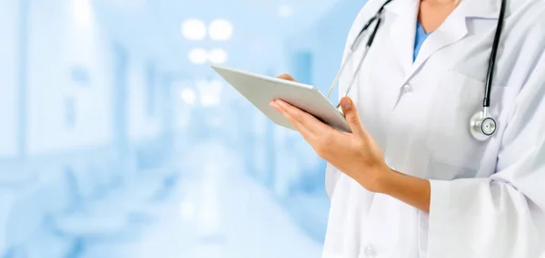 Doctor writing A doctor in a white coat with a stethoscope around their neck uses a tablet to review a report in a hospital hallway.