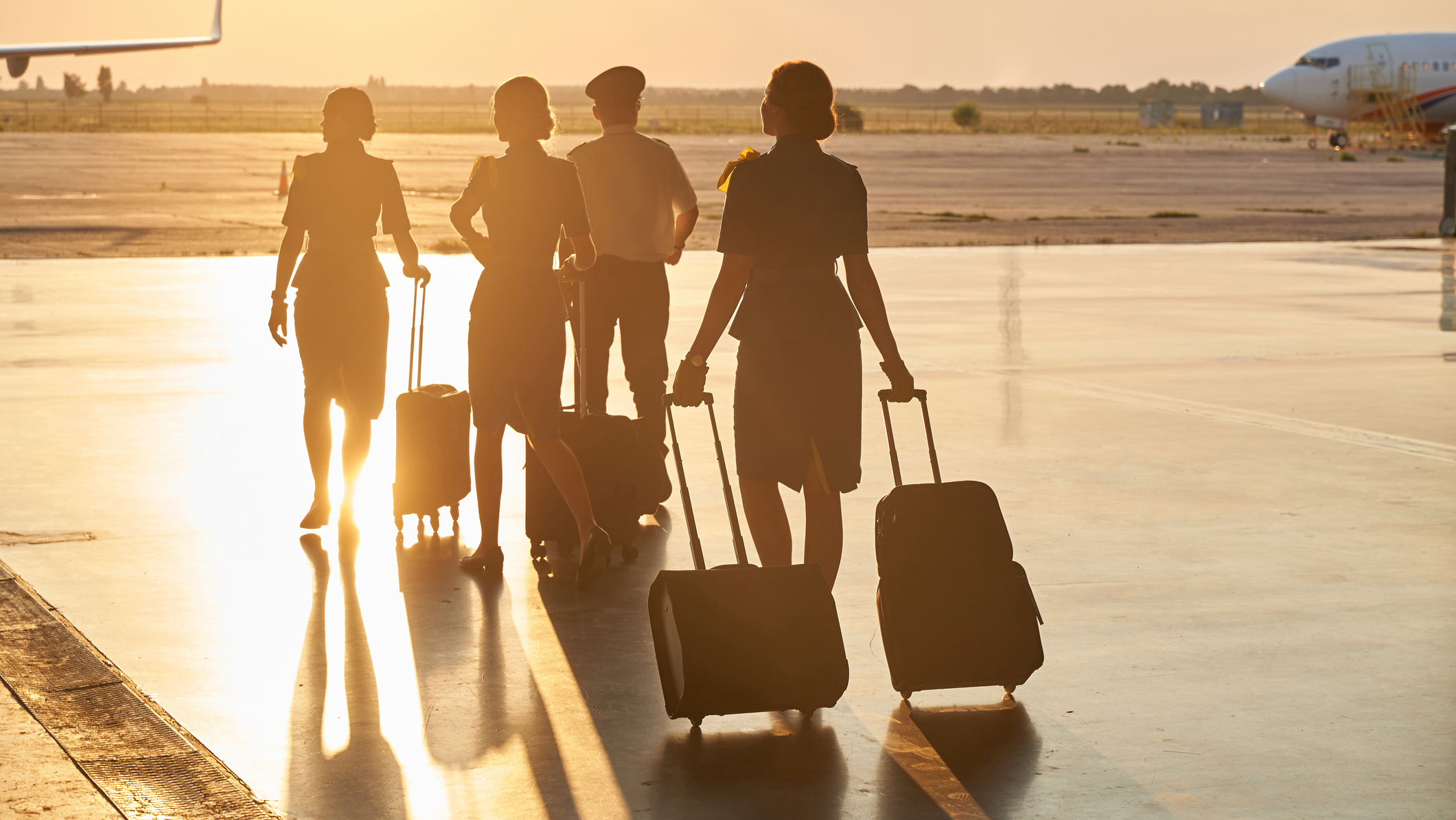 1277750450 Aircrew members carrying their luggage while walking towards a plane.