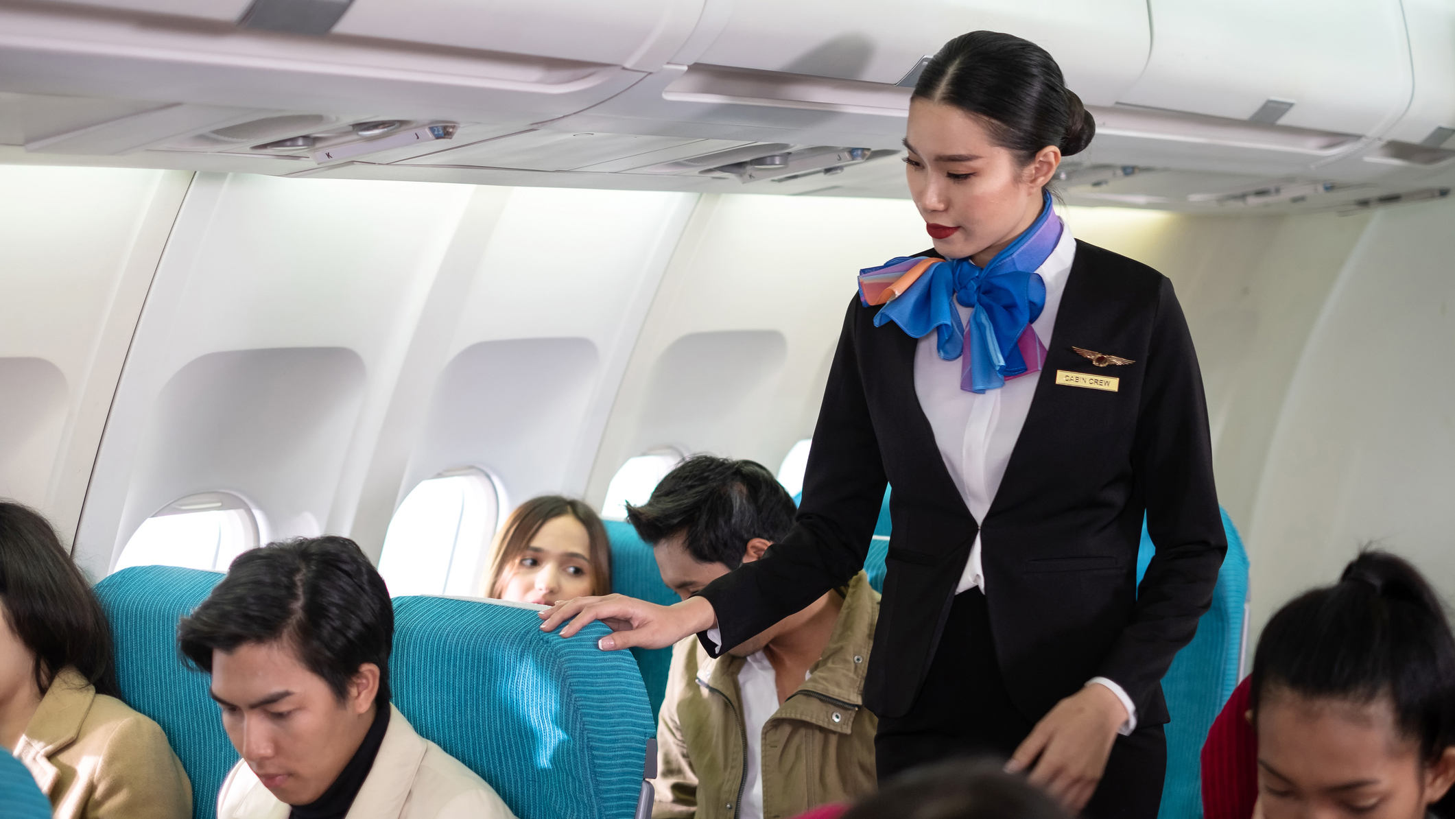 1298634981 Female aircrew member with passengers inside the cabin of a commercial aircraft.