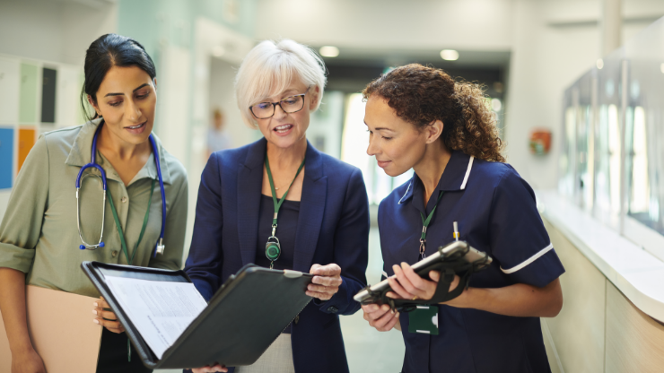 Group discussion Two healthcare workers and an executive look at a folio together in a hospital hallway.