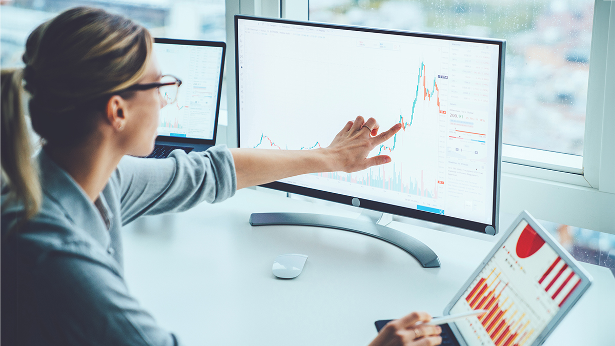 Data analysis on computer Woman in glasses compares line graph on a computer monitor to bar graph on a laptop screen.