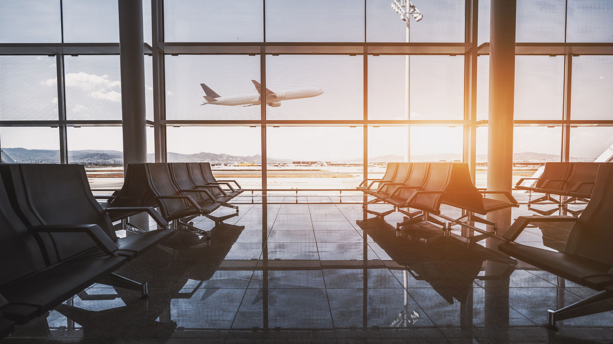 1153101440 A commercial aircraft taking off viewed through the windows of an airport.