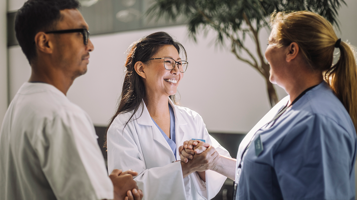 Campaign Background 2 Two healthcare workers clasp hands in friendship while smiling.