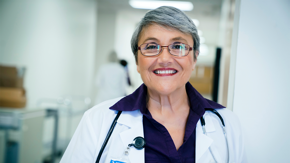 Create inclusive communication image 1 Portrait of an older physician with short graying hair standing in a healthcare facility.