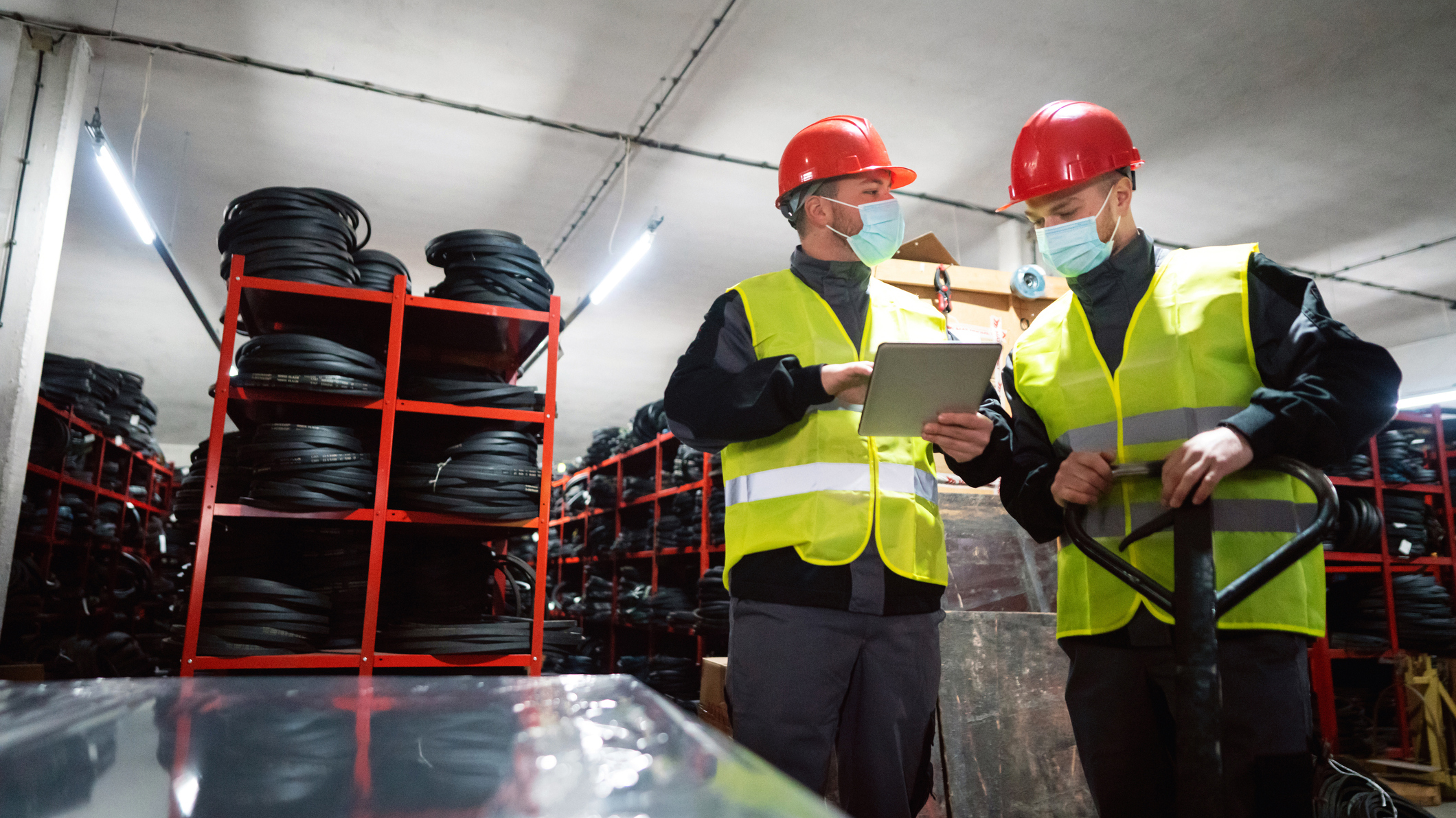 1298924655 Two workers wearing PPE look over papers on a clipboard in an industrial setting.