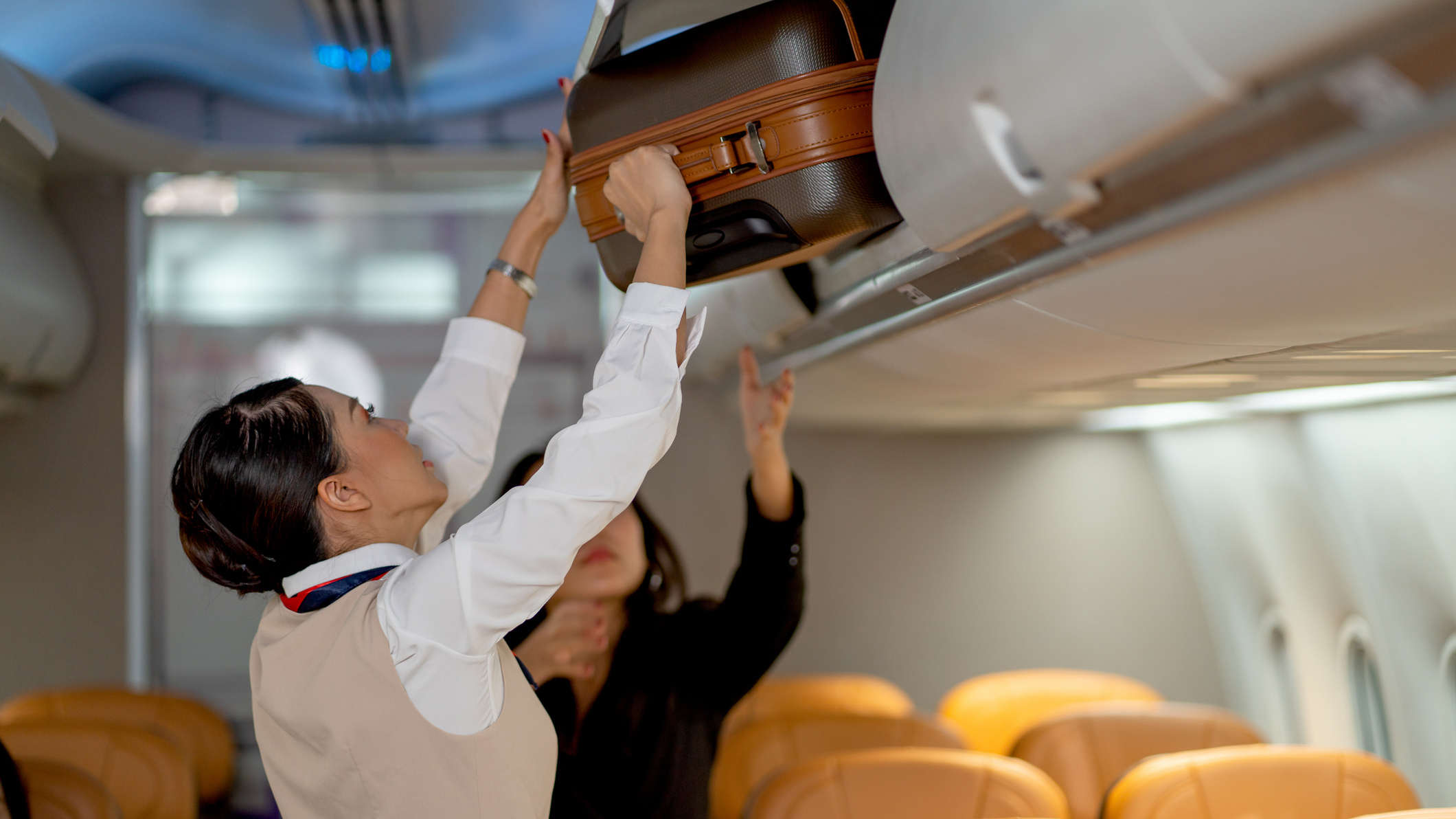 1389718346 Aircrew members securing carryon baggage in an overhead compartment.