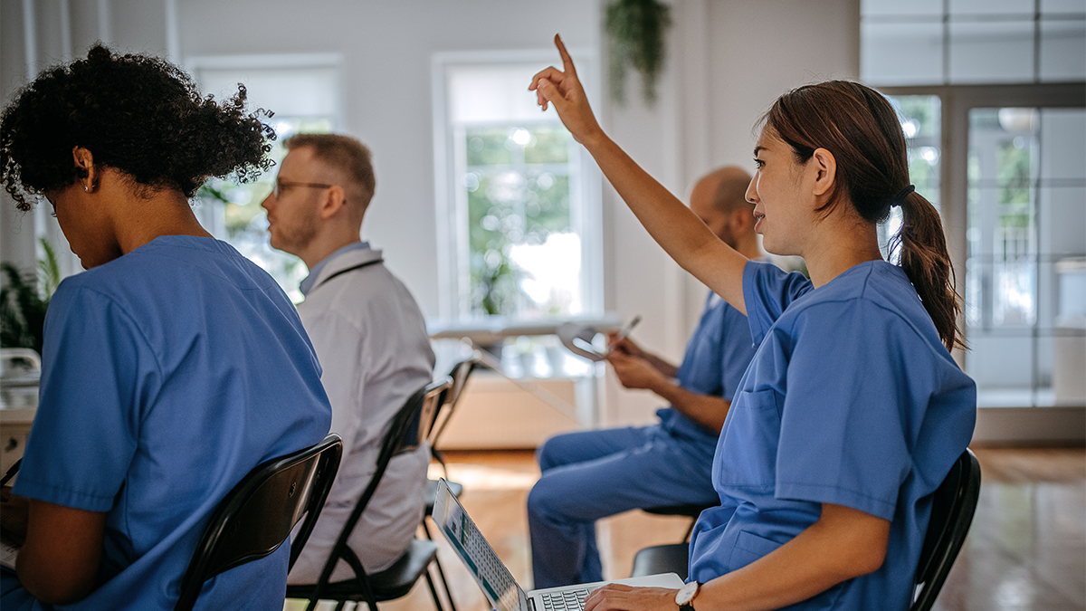 Hearing Your Healthcare Workers 1 Woman in scrubs raises her hand at a healthcare worker town hall meeting.