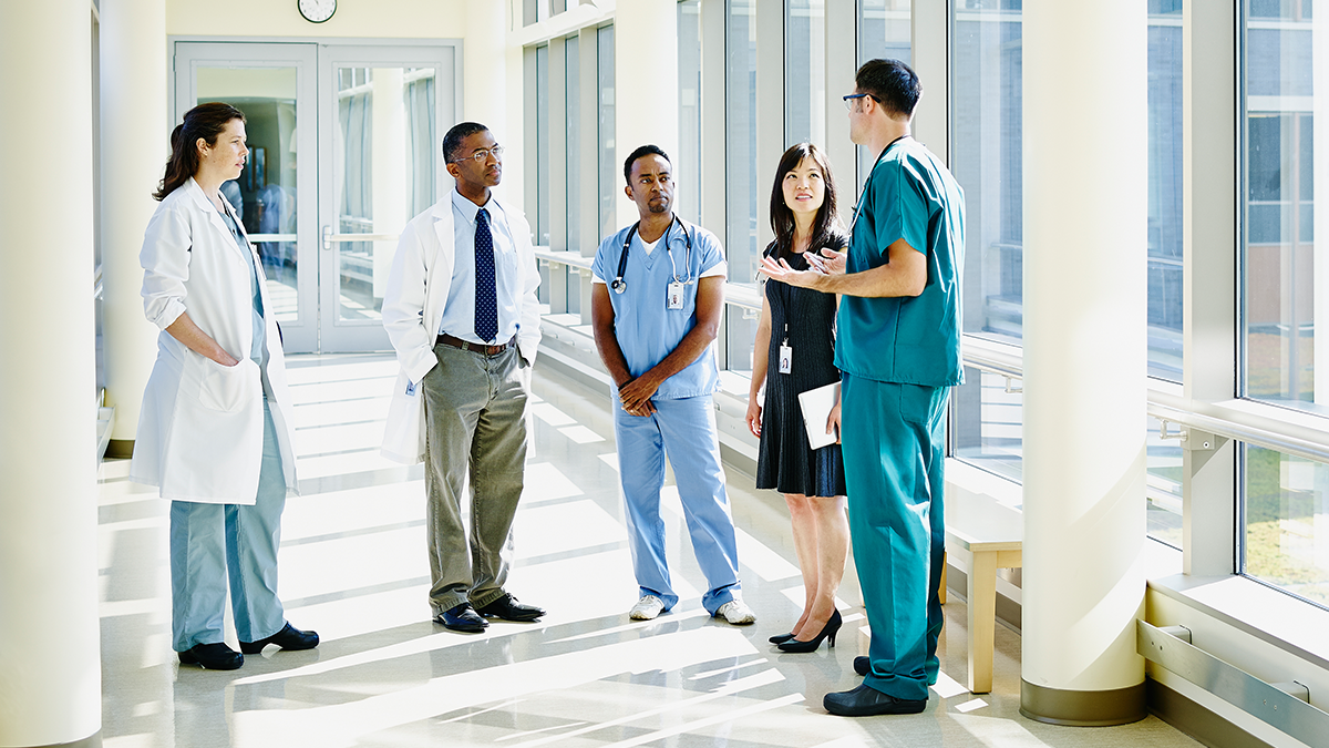 Hearing Your Healthcare Workers 2 Group of diverse healthcare workers having a conversation in a hospital hallway.