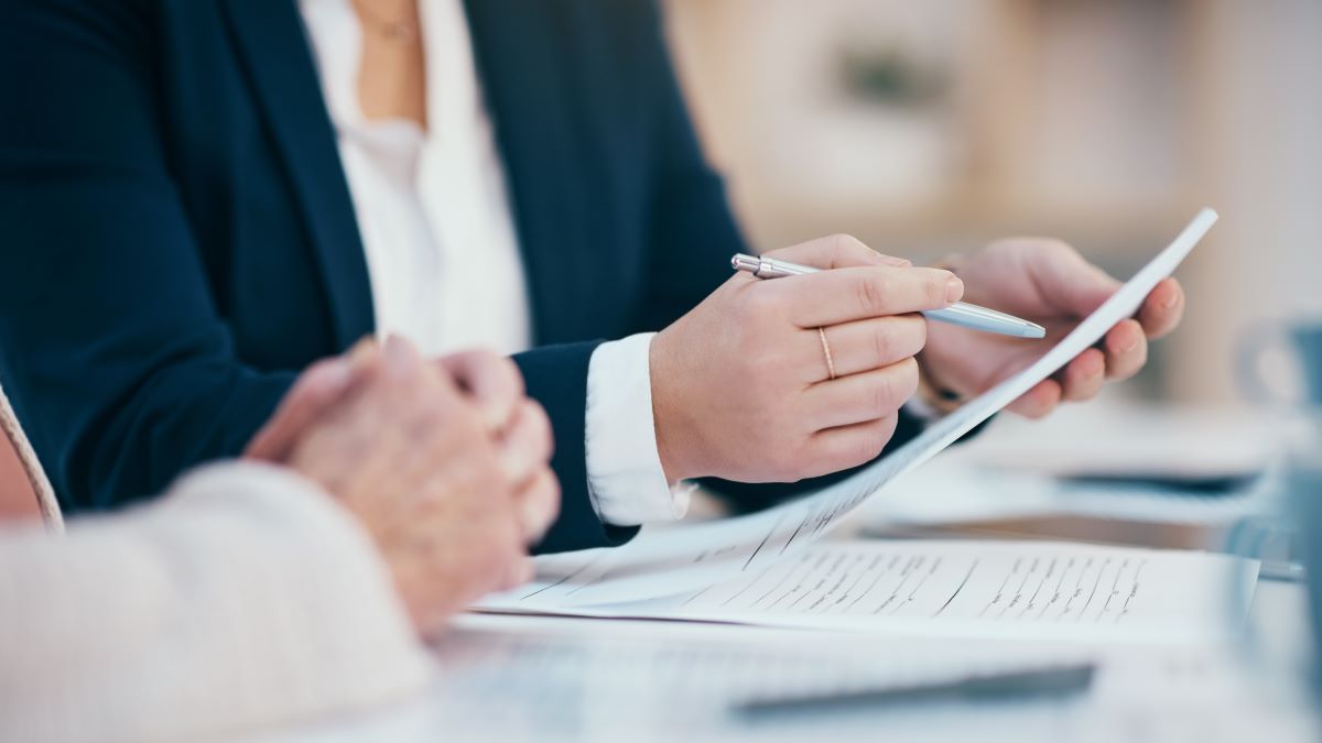 Regulations thumbnail Close of the hands of a person wearing business attire, as they hold a pen and read an official document.