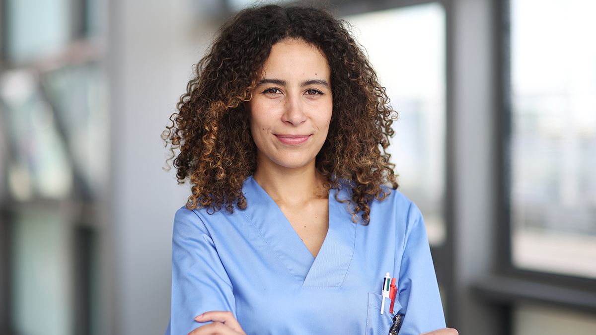 Tips for Stigma Free Comms 1 Healthcare worker in scrubs stands with arms crossed looking confident.