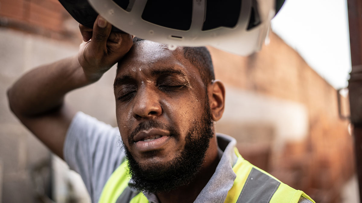 Heat Related Illness African American male construction worker sweating while taking a rest break on a construction site.