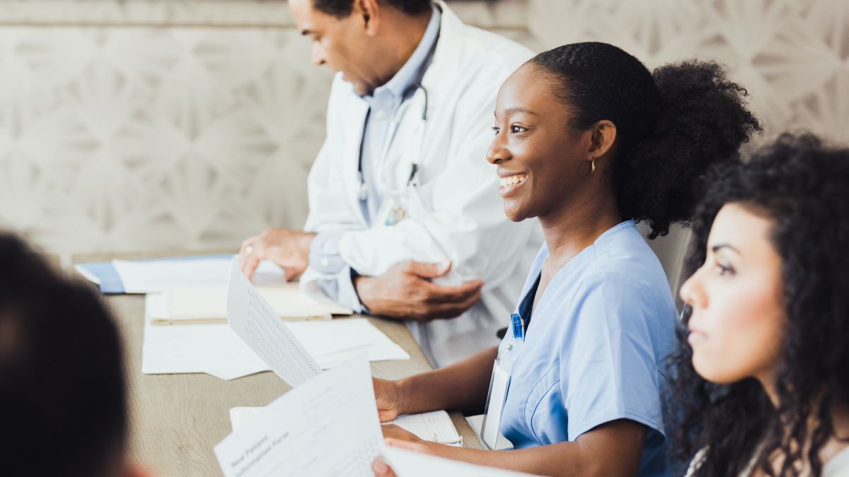 Action 2 case study Smiling African American in scrubs sits at conference table with other healthcare providers.