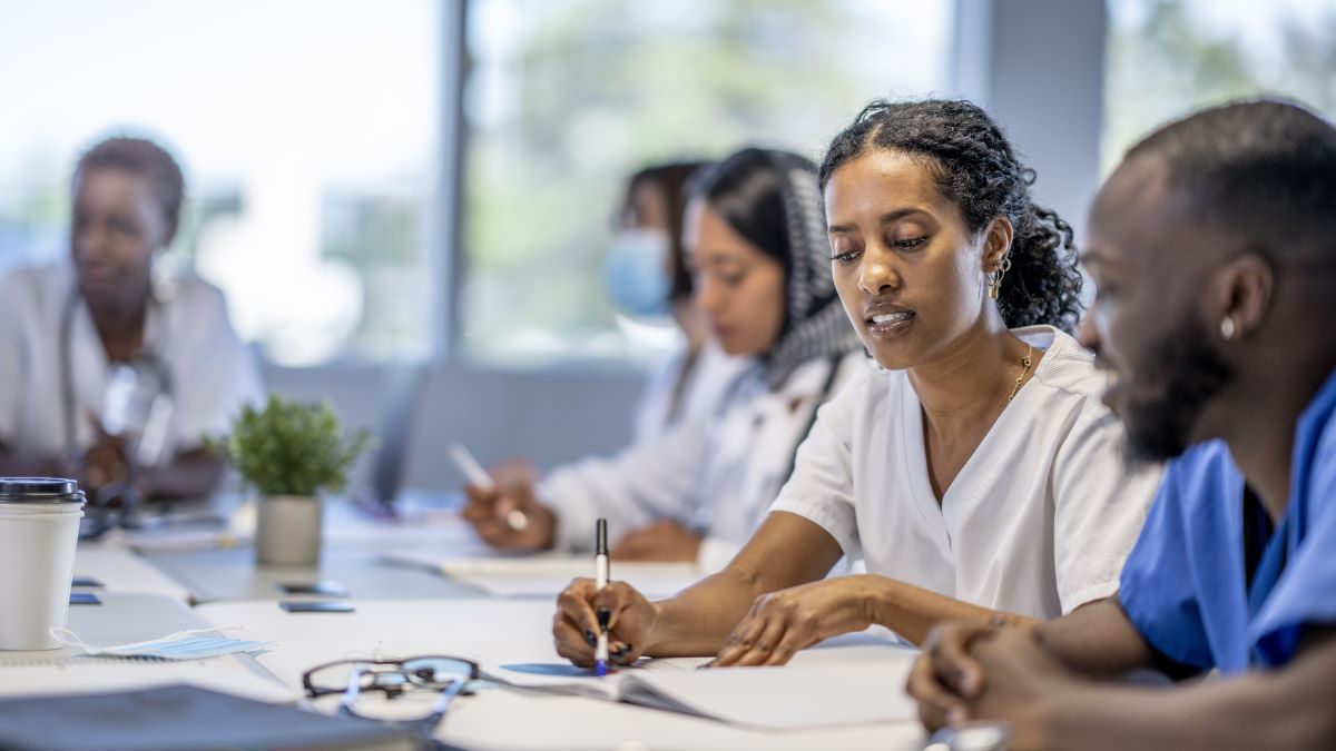 Action 6 case study African American woman in scrubs collaborates with multicultural colleagues at conference table.