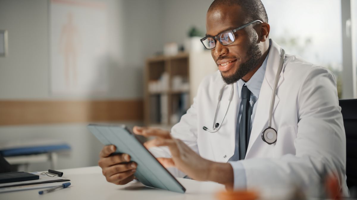 Action 5 case study African American man in a shirt, tie, and physician's coat smiles slightly as he uses a tablet.