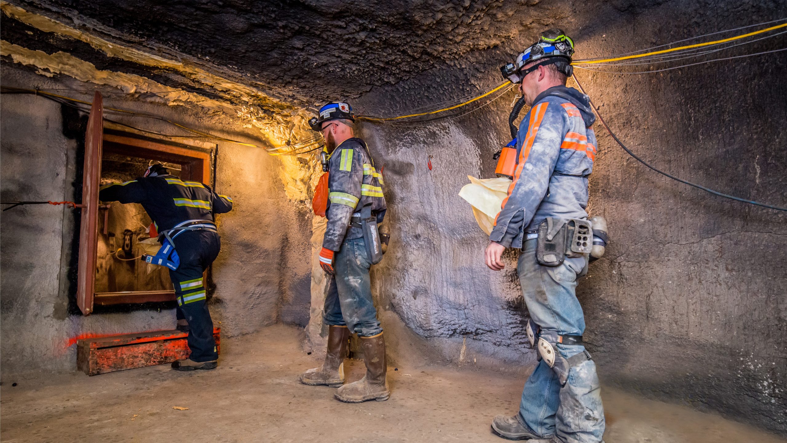 Three miners entering a built-in-place underground refuge wearing SCSRs.