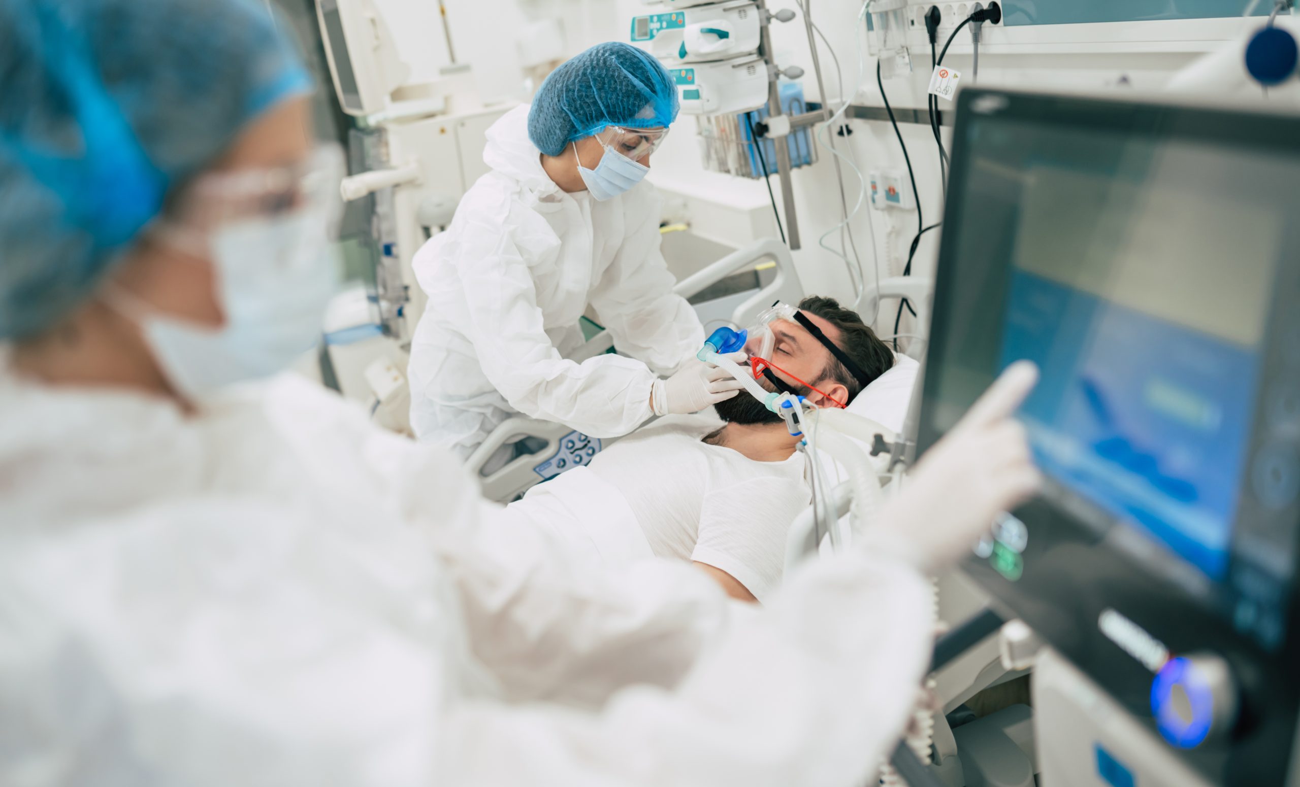 Coronavirus covid-19 infected patient in a quarantine ward at the hospital with doctors in protective suits while they are making disease treatment of him.