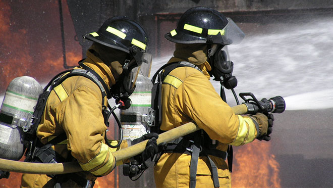 Two firefighters holding a hose and spraying water onto a fire. The firefighters are wearing open-circuit SCBAs.