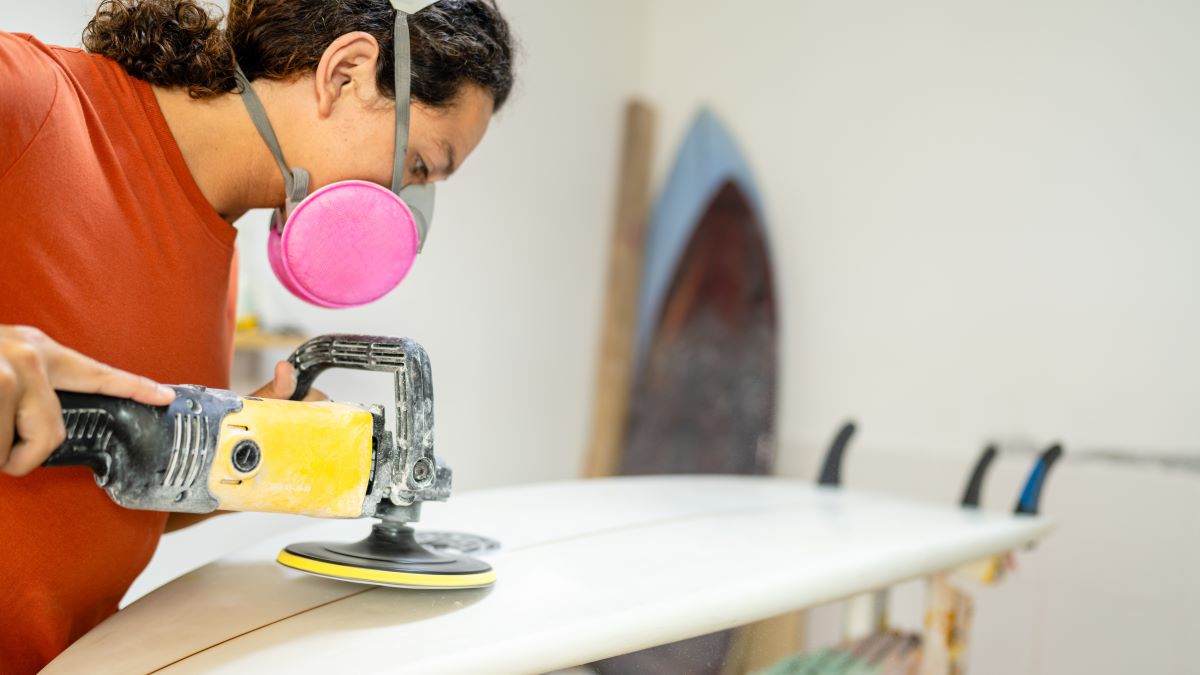Worker wearing an EHMR while sanding the bottom of a surfboard.