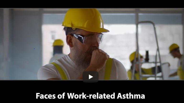 A male construction worker coughing with other workers in the background.