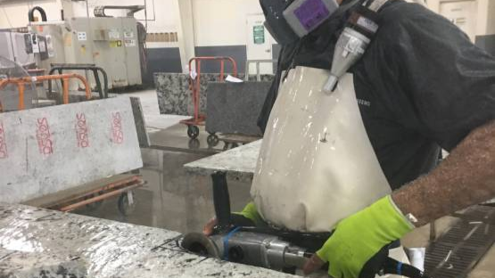 — title missing — Worker cutting stone countertop using wet method.