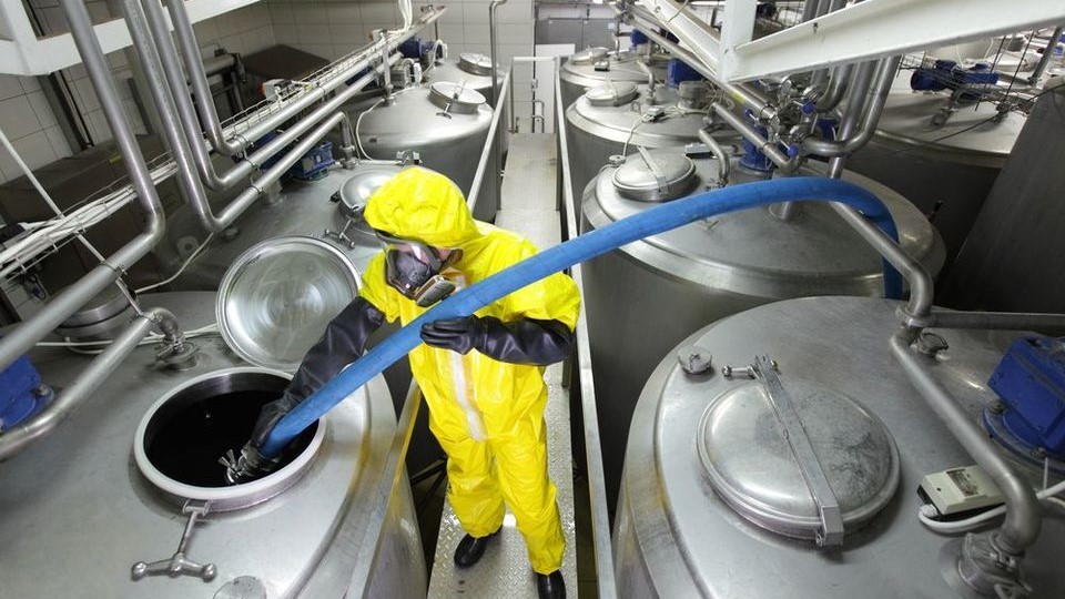 Chemical manufacturing worker chemical manufacturing worker in a yellow suit handling chemicals in a large steel canister