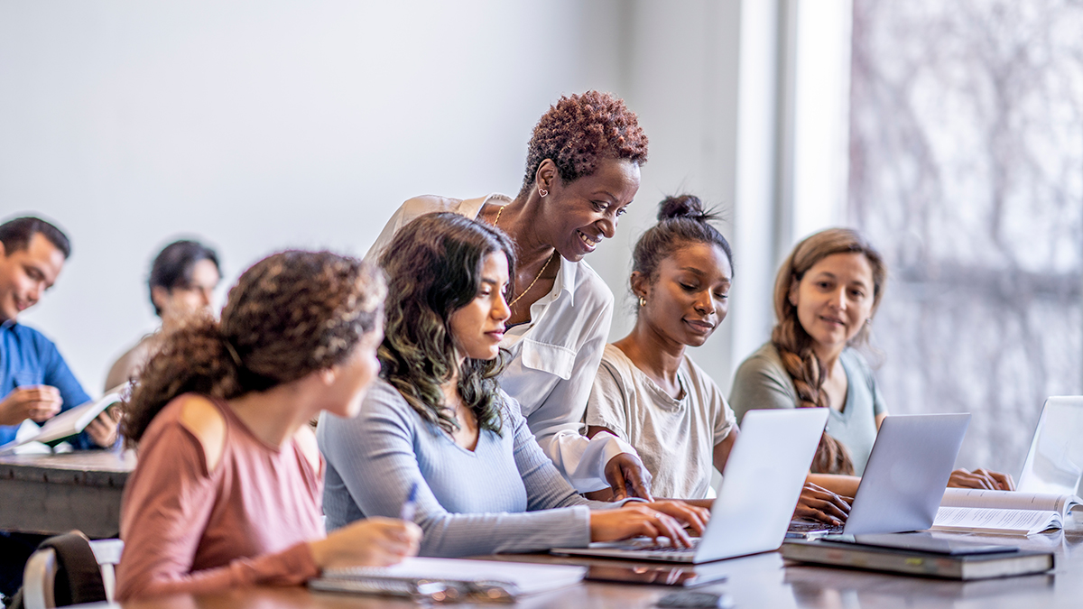 — title missing — Four students with laptops interact with professor