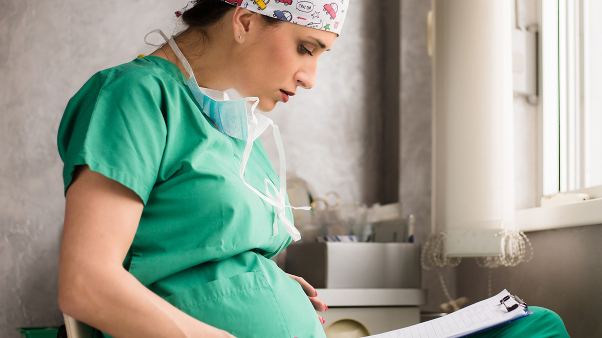 1145455957 Pregnant healthcare worker reading a chart on a clipboard.