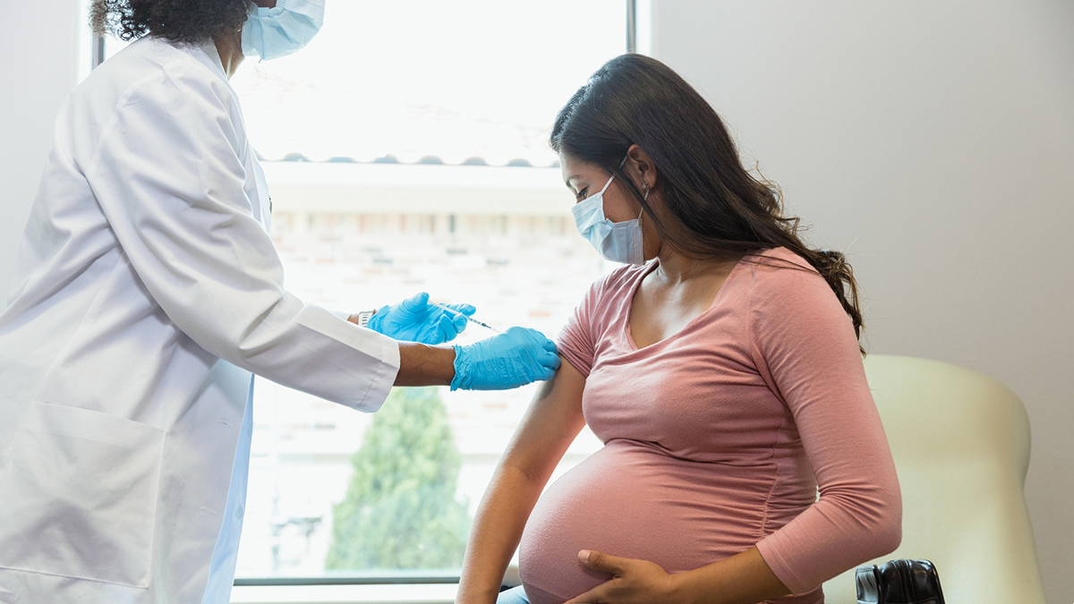 1340094898 Female healthcare provider working with a pregnant patient, both wearing PPE.