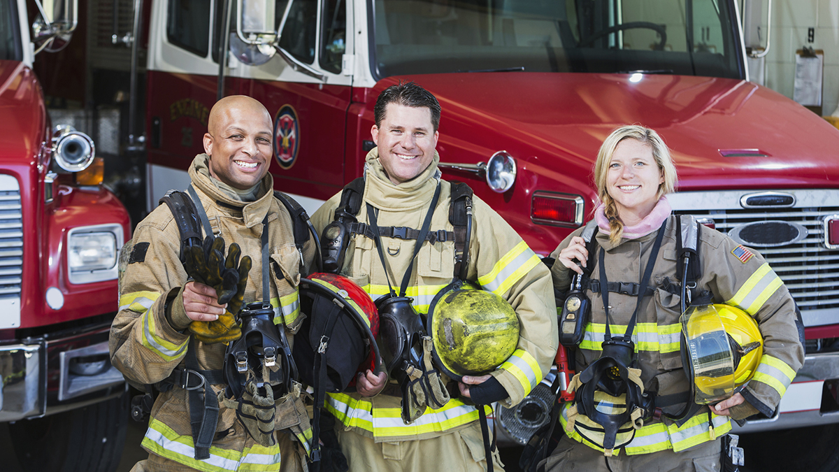 473421900 Group of structural firefighters standing in front of trucks with gear