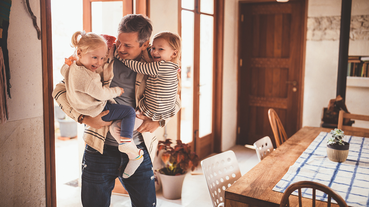 thumbnail A father has returned home from work and is holding 2 children.