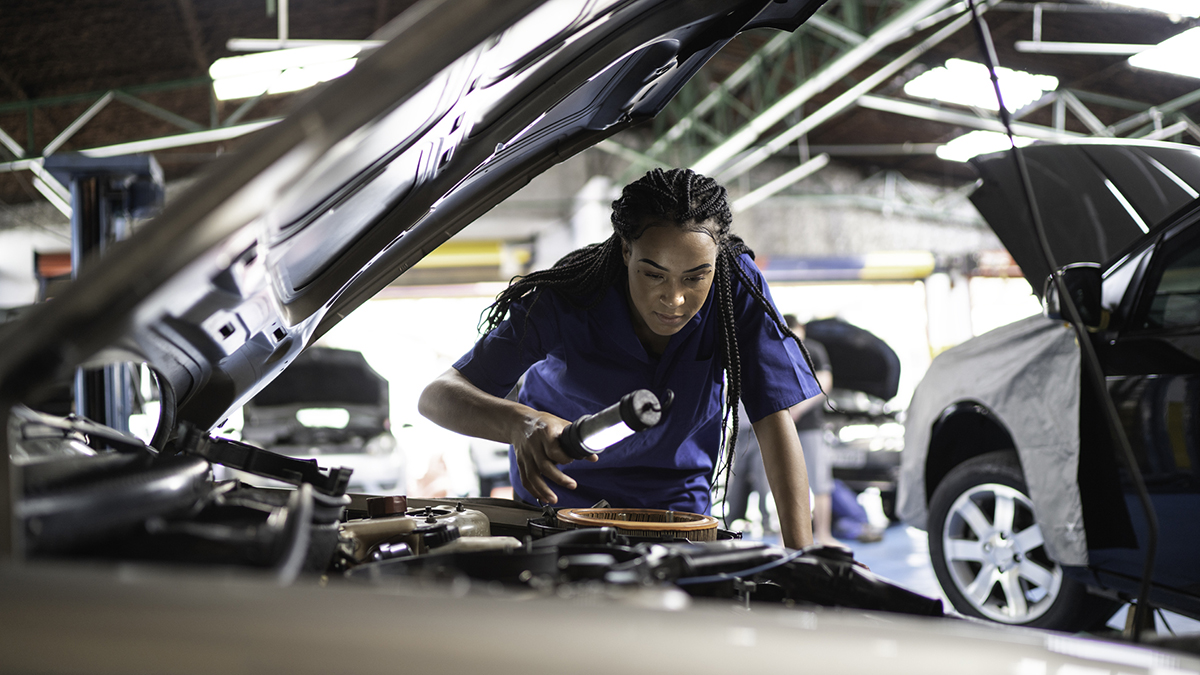 — title missing — An automobile service worker inspects and engine compartment with a light.
