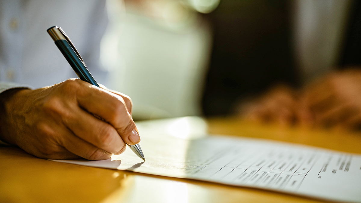 a hand holding a pen writing on a white piece of paper on top of a wooden tabletop